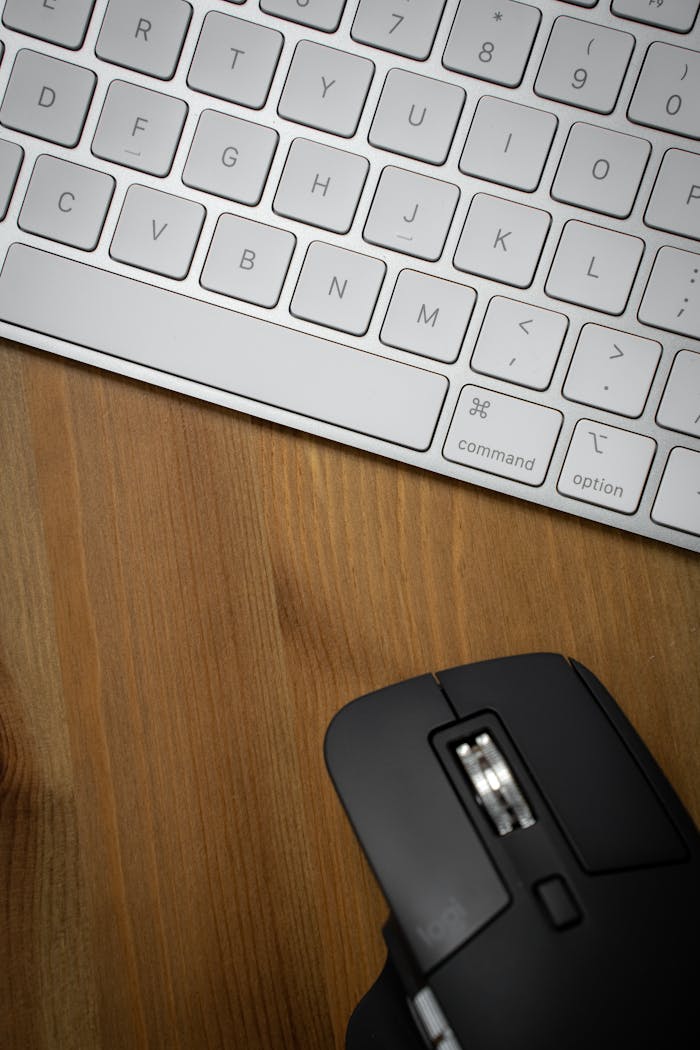 our-services-06 A sleek workspace setup featuring a white keyboard and a black ergonomic mouse on a wooden surface.